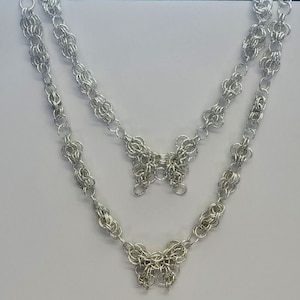 Può includere: Una collana a catena d'argento con due ciondoli a forma di farfalla. La collana è realizzata con piccoli anelli di metallo interconnessi.