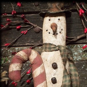 Può includere: Un pupazzo di neve primitivo fatto a mano con una canna di zucchero rosso e bianca, una sciarpa a quadri verdi e un cappello a cilindro nero. Il pupazzo di neve ha un naso di legno marrone e quattro bottoni neri.