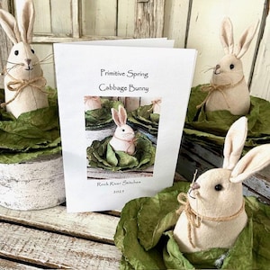 May include: A pattern for a primitive spring cabbage bunny, with a photo of a finished bunny in a cabbage. The pattern is titled "Primitive Spring Cabbage Bunny" and is by Rock River Stitches 2023.