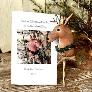 May include: A craft pattern for a primitive Christmas horse reindeer ornament. The pattern is titled "Primitive Christmas Hobby Horse Reindeer Ornie" and is from Rock River Stitches 2024.