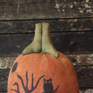 May include: A handmade orange fabric pumpkin with a green fabric stem and black painted details. The pumpkin has a black silhouette of an owl and a crescent moon with a hand reaching out from behind it.