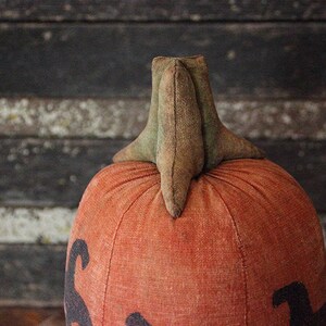 May include: A handmade orange fabric pumpkin with a green felt stem. The pumpkin has a stitched design on the front.