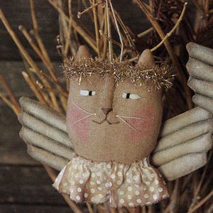 May include: A handmade fabric cat angel ornament with a brown body, white wings, and a white polka dot dress. The cat has a gold glitter halo and a pink face.