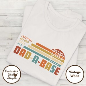 May include: White t-shirt with a retro-style graphic that says "I keep all my dad jokes in a dad-a-base". The graphic features a floppy disk in a rainbow color scheme.