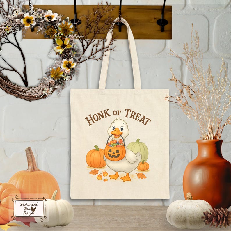 May include: A cream-colored tote bag with the words "Honk or Treat" printed in brown. The bag features a cartoon duck holding a jack-o'-lantern bucket, surrounded by pumpkins and candy corn. A fall-themed design.