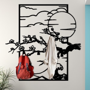 May include: A black metal wall art piece featuring a tree branch design with a full moon, clouds, and a wave. A red backpack and a white jacket hang from the art. A black and wood console table with a plant and vase are in front.