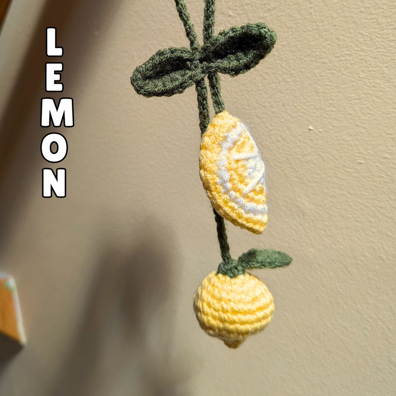 Op de afbeelding: Een gehaakte citroenenkrans met groene bladeren en gele citroenen. De citroenen hebben witte stiksels om de binnenkant van een citroen na te bootsen.