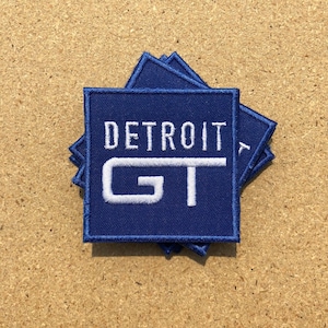 May include: A stack of blue fabric patches with white embroidered text that reads "DETROIT GT".