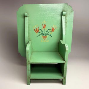 May include: A small, vintage, green wooden chair with a shelf and a fold-down table. The chair back features a hand-painted floral design with orange and yellow tulips in a vase. The chair is painted in a light green color.