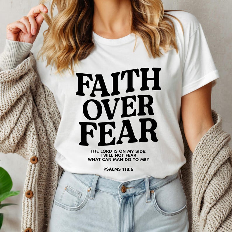 Może przedstawiać: Biała koszulka z czarnym nadrukiem "FAITH OVER FEAR" i wersetem "THE LORD IS ON MY SIDE: I WILL NOT FEAR WHAT CAN MAN DO TO ME? PSALMS 118:6"