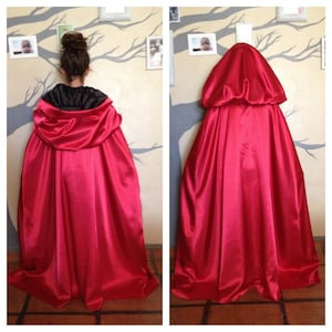 May include: A red satin cape with a large hood. The cape is draped over a chair and the hood is pulled up.
