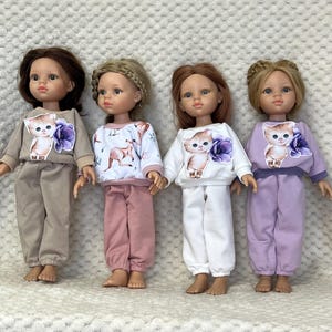 May include: Four dolls dressed in coordinated outfits. Each doll has a unique hairstyle and hair colour. The outfits consist of a sweatshirt featuring a cat design and trousers. The outfits are in shades of beige, pink, white, and lilac.