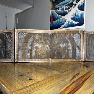 Op de afbeelding: Een houten tafelblad spelscherm met vijf panelen, elk met een ander beeld van een kerkerscène. De panelen zijn met scharnieren verbonden en kunnen worden opgevouwen voor opslag.