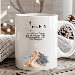 May include: White ceramic mug with a black and white illustration of a cross on a rocky path leading to a body of water. The mug has the text "John 14:6" and the quote "Jesus said to him, I am the way the truth and the life. No one comes to the father except through me."