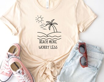 May include: A beige t-shirt with a black graphic of a palm tree, sun, and waves. The text "Beach More Worry Less" is printed below the graphic.