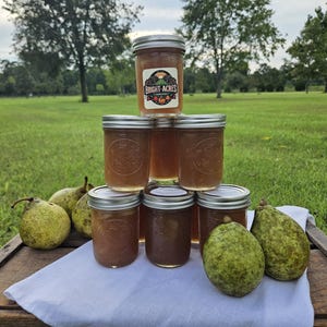 May include: A stack of six glass jars filled with a light brown substance, likely jam or preserves. The jars are labeled "Bright Acres".  The jars are arranged in a pyramid shape on a wooden surface.  There are several green pears in front of the jars.
