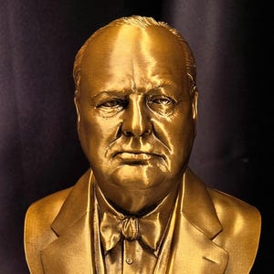 Peut inclure: Buste doré d'un homme en costume et nœud papillon. La sculpture présente un visage détaillé et est montée sur une base noire. Le buste est placé sur un fond sombre.