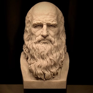 May include: A beige bust of a man with a long beard and hair. The sculpture has a stern expression and is set against a dark background. The bust is on a black base.