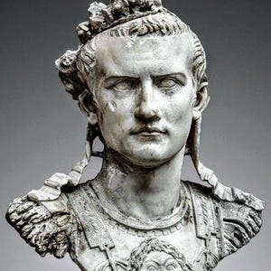 K&ouml;nnte beinhalten: Eine wei&szlig;e Marmorb&uuml;ste einer Person mit einem Bl&auml;tterkranz und einer R&uuml;stung. Der Brustpanzer zeigt ein zentrales Relief eines Gesichts. Die Figur hat einen ernsten Ausdruck, markante Gesichtsz&uuml;ge und B&auml;nder, die seitlich am Kopf herabh&auml;ngen.