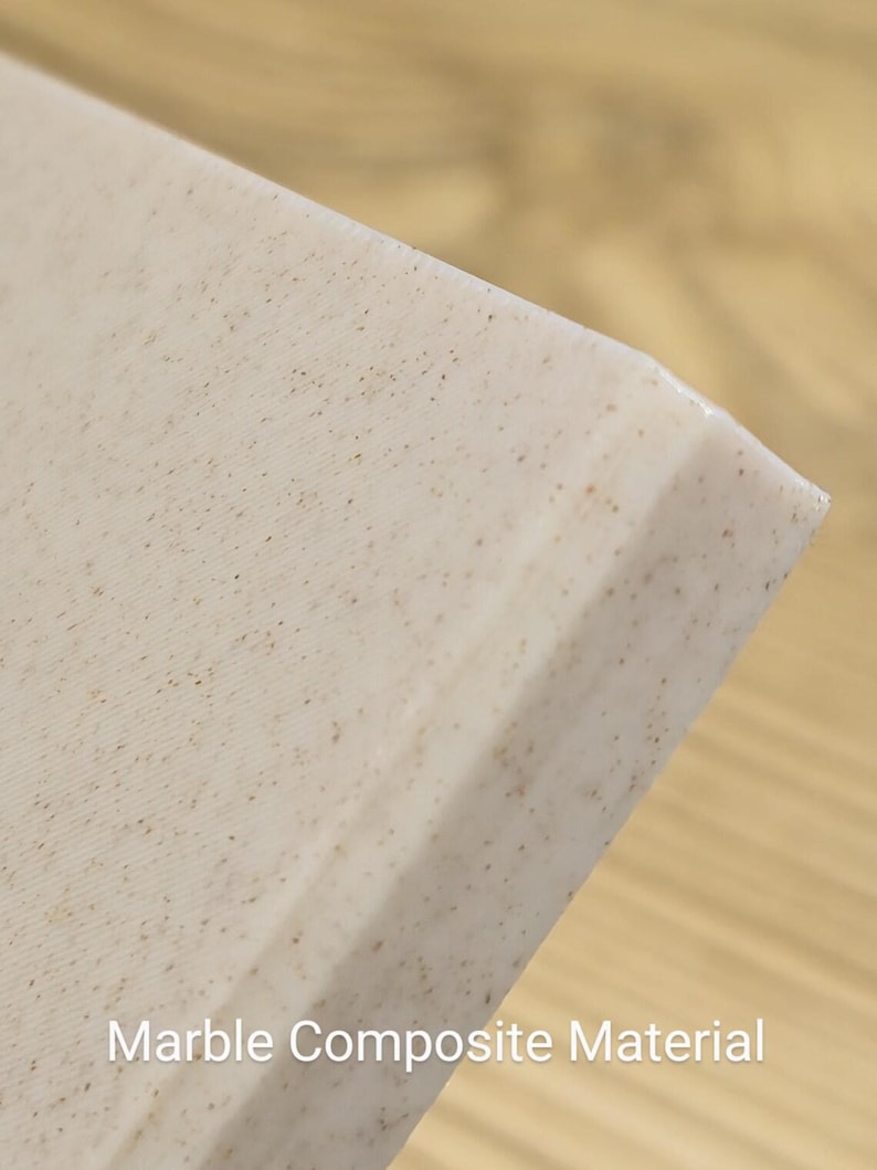 K&ouml;nnte beinhalten: Ein Eckabschnitt einer Platte aus cremefarbenem Marmor-Verbundwerkstoff mit feinen braunen Sprenkeln auf der gesamten Oberfl&auml;che. Das Material hat eine glatte, matte Oberfl&auml;che und eine saubere, gerade Kante, mit dem Text Marble Composite Material.