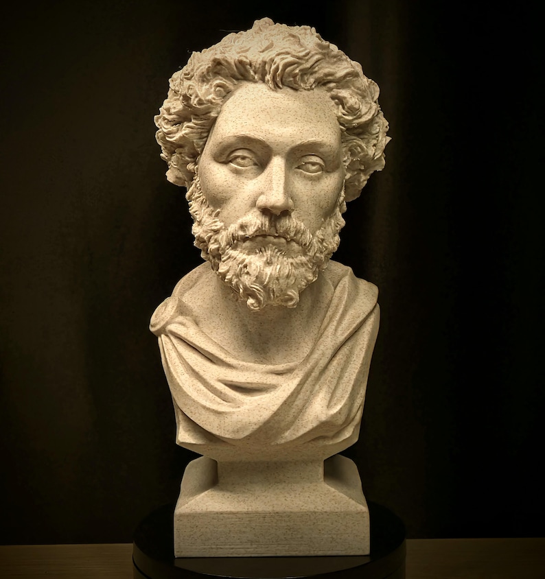 May include: A detailed bust sculpture of a man with curly hair and a full beard. The sculpture is light beige with a textured surface, and the subject is draped in a toga. The bust is mounted on a square base.