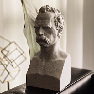 May include: A gray stone bust sculpture of a man with a mustache. The bust is on a black surface.