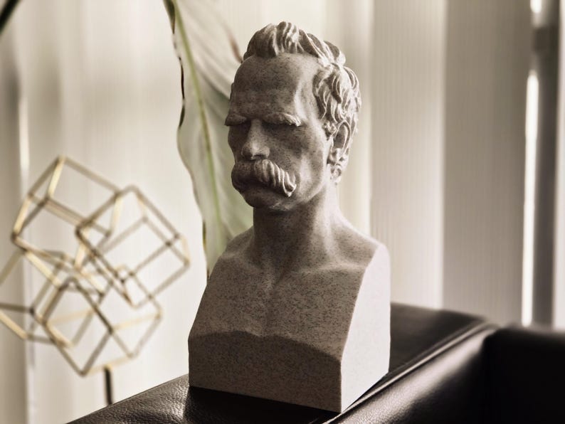May include: A gray stone bust sculpture of a man with a mustache. The bust is on a black surface.