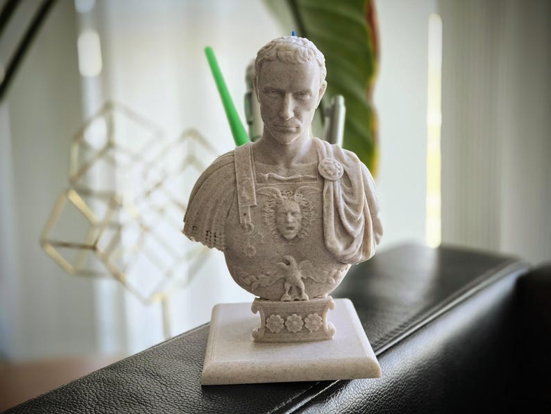 May include: A beige Roman emperor bust, with intricate details of the face and clothing. The sculpture sits on a square base with floral patterns. This decorative item is likely for home decor, and is measured in centimeters.