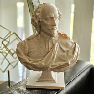 May include: A white bust sculpture of William Shakespeare, the famous playwright, poet, and actor. The bust is on a white pedestal and is made of a smooth, textured material.