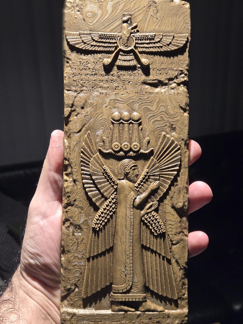 May include: A rectangular, tan-coloured relief carving featuring two detailed figures. The top figure is a winged symbol, and the bottom figure is a winged person with arms outstretched. The carving has a textured, layered appearance.