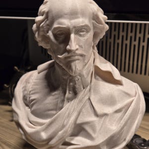 May include: A white 3D printed bust of William Shakespeare. The bust is detailed and shows Shakespeare's face and shoulders. The bust is on a white base.