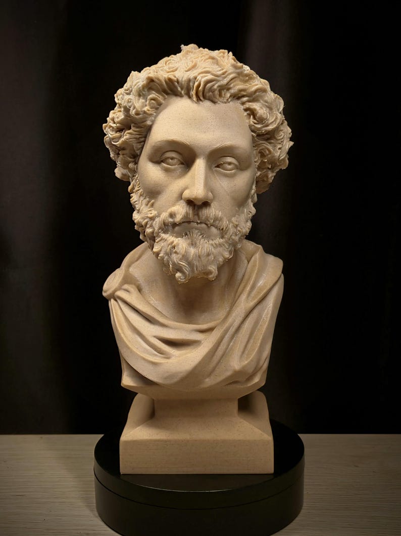 May include: A beige-colored bust sculpture of a man with curly hair and a beard. The sculpture features a draped garment over the shoulders and is mounted on a square base. The bust is set against a dark background.