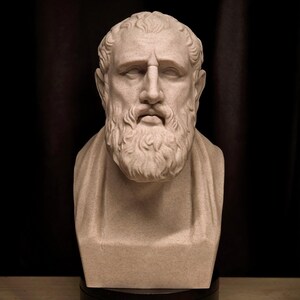 May include: A beige bust of a man with a beard and curly hair. The sculpture has a serious expression and is set against a dark background. The bust is a classical art piece.