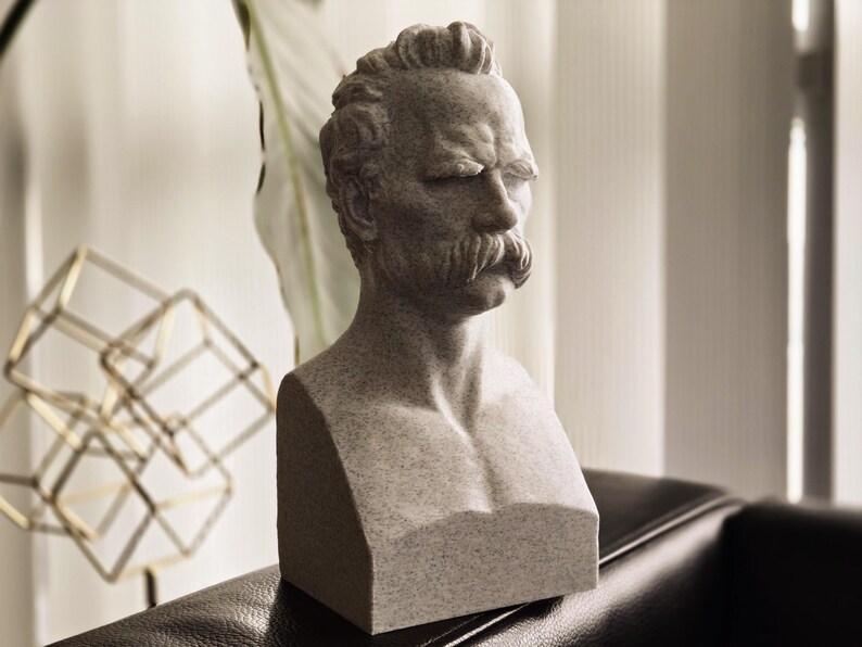 May include: A gray stone bust sculpture of a man with a mustache. The bust is detailed with realistic features and a textured surface.