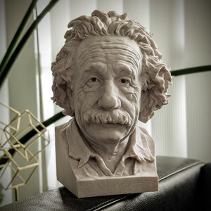 May include: A detailed bust of Albert Einstein, sculpted in a light beige stone. The sculpture captures Einstein's iconic hairstyle, mustache, and facial features. The bust is set on a rectangular base, showcasing the scientist's likeness.