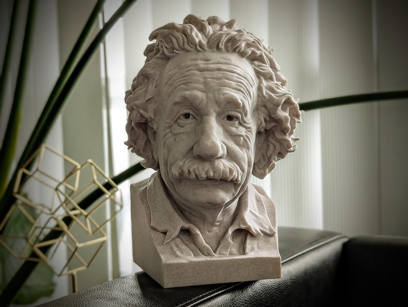 May include: A detailed bust of Albert Einstein, sculpted in a light beige stone. The sculpture captures Einstein's iconic hairstyle, mustache, and facial features. The bust is set on a rectangular base, showcasing the scientist's likeness.