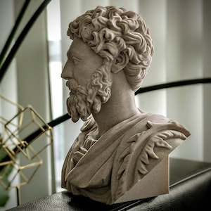 May include: A detailed bust of a man with curly hair and a beard, sculpted in a light beige stone. The sculpture features a draped garment and is set against a blurred background with greenery and geometric decor.