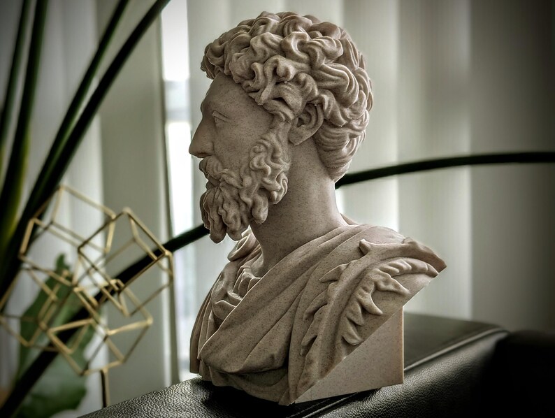 May include: A detailed bust of a man with curly hair and a beard, sculpted in a light beige stone. The sculpture features a draped garment and is set against a blurred background with greenery and geometric decor.