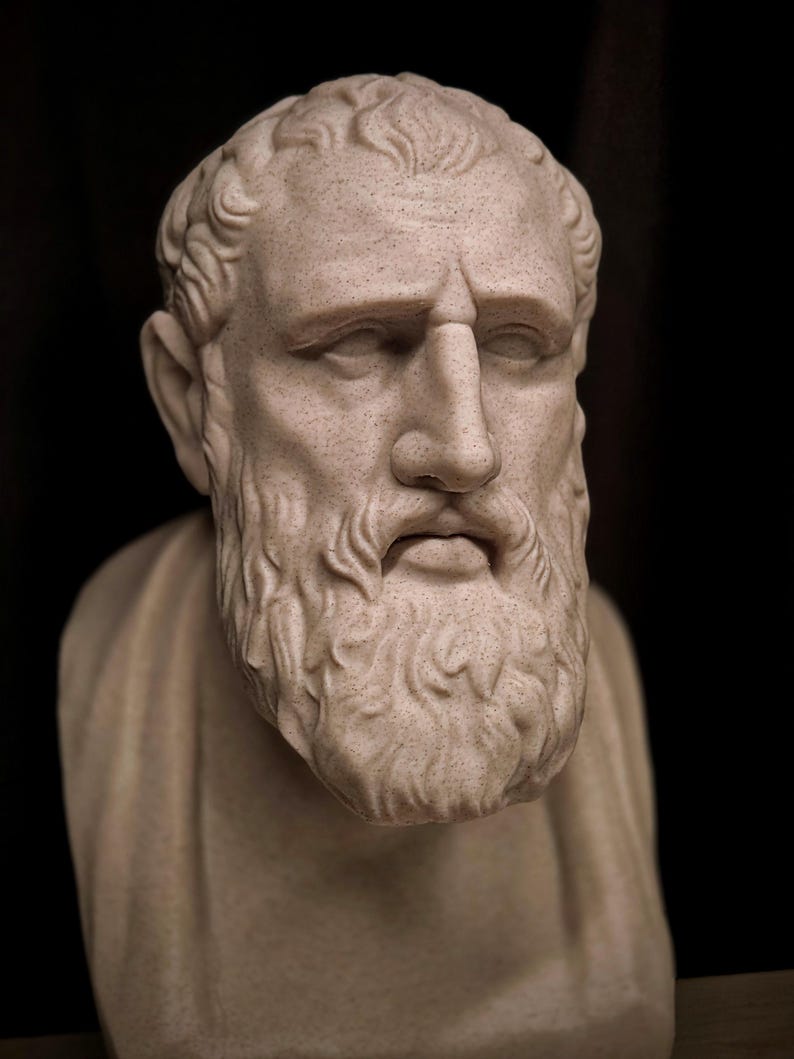 May include: A light beige bust of a man with a full beard and curly hair. The sculpture is set against a black background. The man has a serious expression. The sculpture is a classical style.