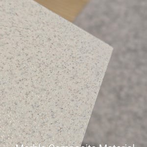 May include: Close-up of a white marble composite material with a speckled texture. The material is smooth and has a subtle shimmer.