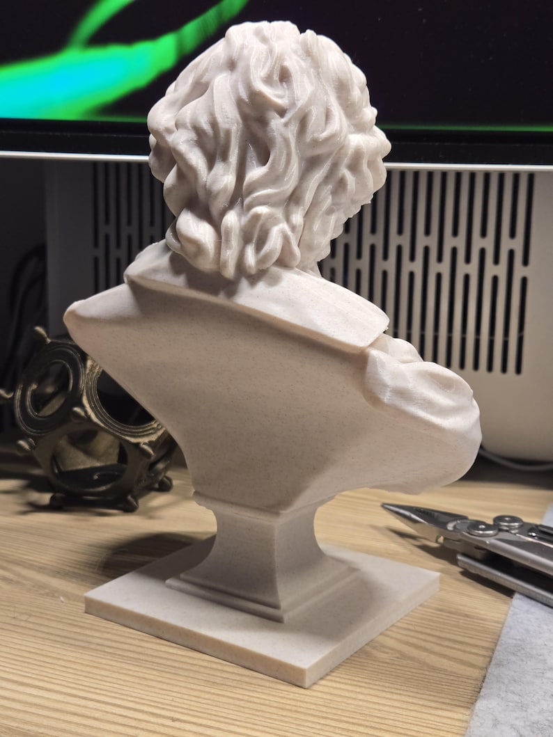 May include: A white plaster bust of a person with curly hair. The bust is on a square base.