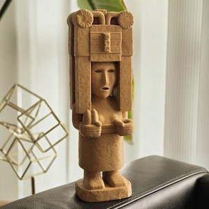 May include: A brown, carved wooden statue of a person wearing a headdress. The statue is standing on a wooden base.
