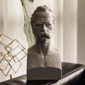 May include: A gray stone bust sculpture of a man with a mustache. The sculpture is on a dark brown surface.