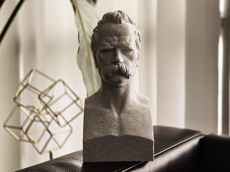 May include: A gray stone bust sculpture of a man with a mustache. The sculpture is on a dark brown surface.