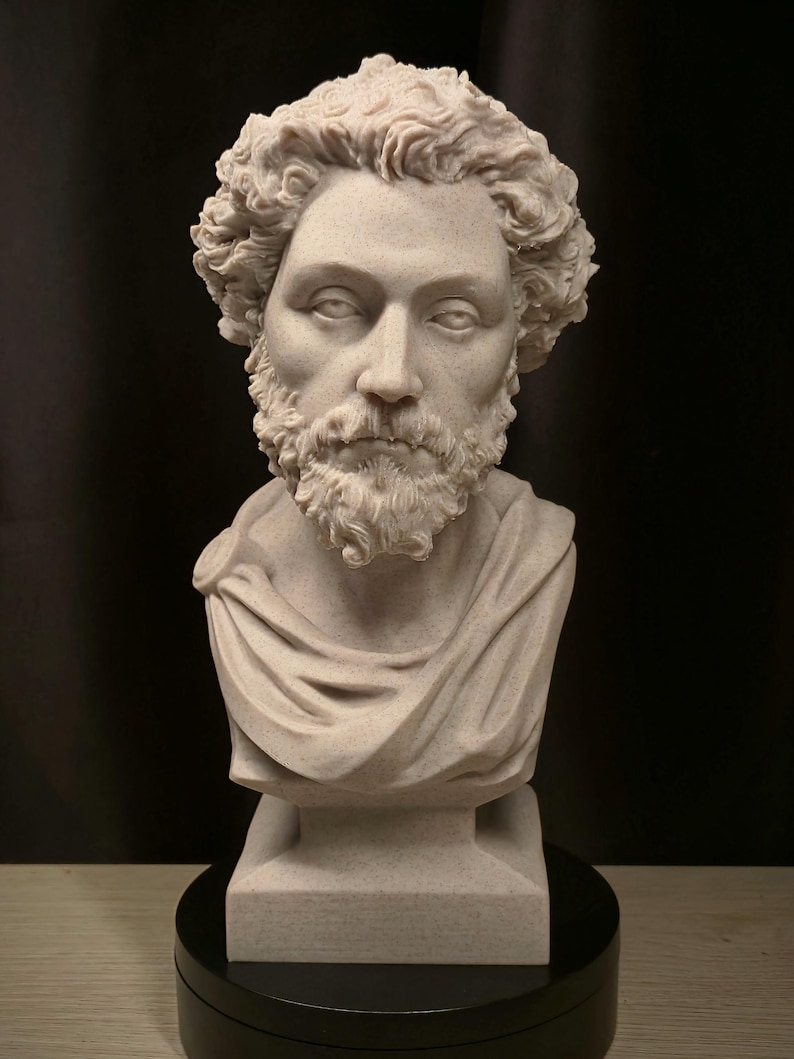 May include: A detailed bust sculpture of a man with curly hair and a beard. The sculpture is light beige and features a draped garment over the shoulders. It is mounted on a black base, set against a dark background.