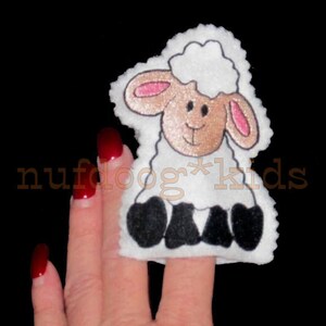 May include: White felt finger puppet shaped like a sheep with black hooves and a brown face. The sheep has a white fluffy head with pink ears and a black nose.