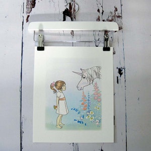 May include: A rectangular art print featuring a line drawing of a child with a ponytail wearing a white dress, holding a green apple behind their back, facing a unicorn. The scene includes colourful flowers and small blue figures in the grass.