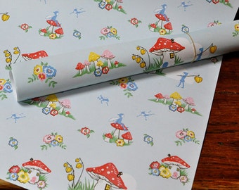 May include: A light blue wrapping paper roll featuring a repeating pattern of red and white mushroom houses, small blue fairy figures, yellow lantern-like flowers, and clusters of colorful blossoms in red, yellow, and blue hues.