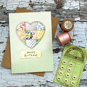 Può includere: Biglietto di auguri di compleanno fatto a mano con un design a cuore patchwork. Il biglietto è verde chiaro con una busta marrone. Anche rocchetti di filo e una scheda di bottoni vintage.