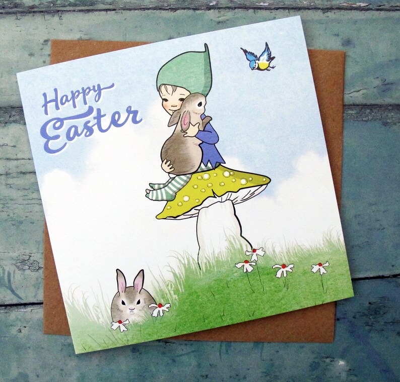 May include: A square greeting card featuring a cartoon illustration of a figure in a green hat sitting on a yellow-spotted mushroom while holding a brown rabbit. The text Happy Easter is printed in blue. A small blue bird and another rabbit are visible.